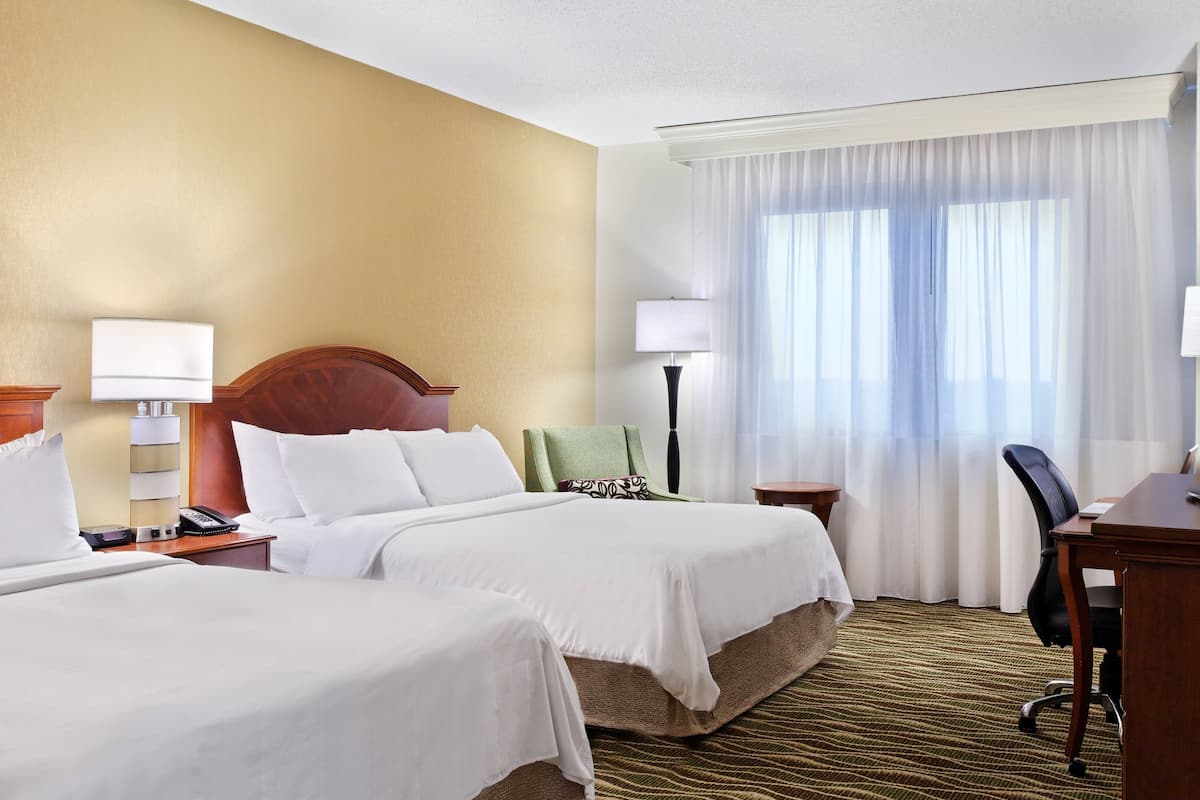 Ein Hotelzimmer mit zwei Betten, einem Schreibtisch, einem Stuhl, einer Lampe und einem Fernseher.