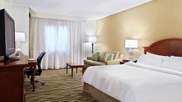 A hotel room with a bed, a desk with a computer, a chair, a lamp, and a window with curtains.