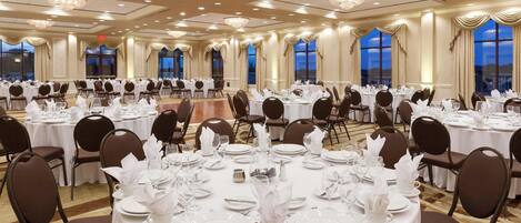 A banquet hall with round tables set for dining, large windows, and chandeliers.