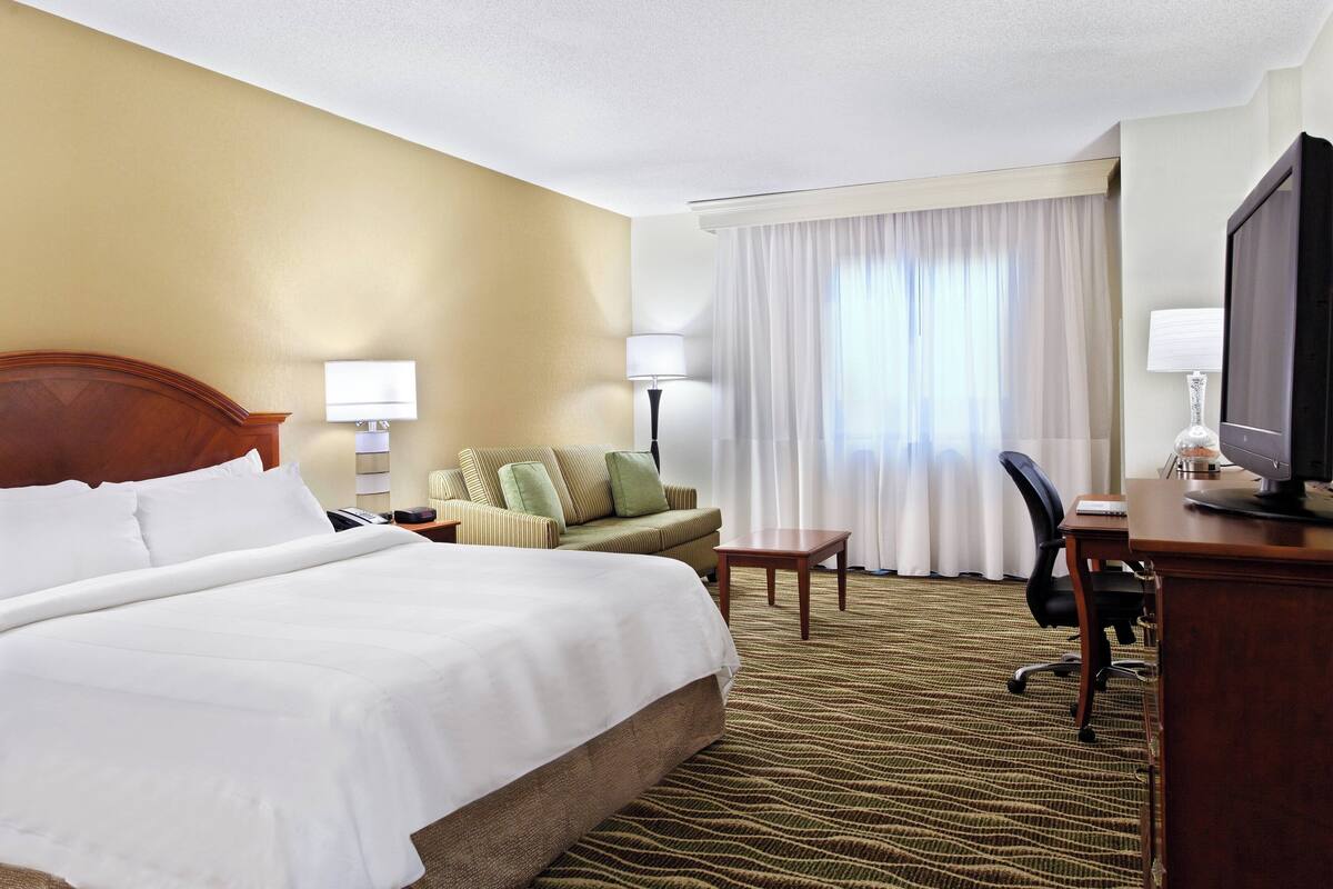 Ein Hotelzimmer mit einem großen Bett, einem Sofa, einem Schreibtisch mit Computer und einem Fernseher.