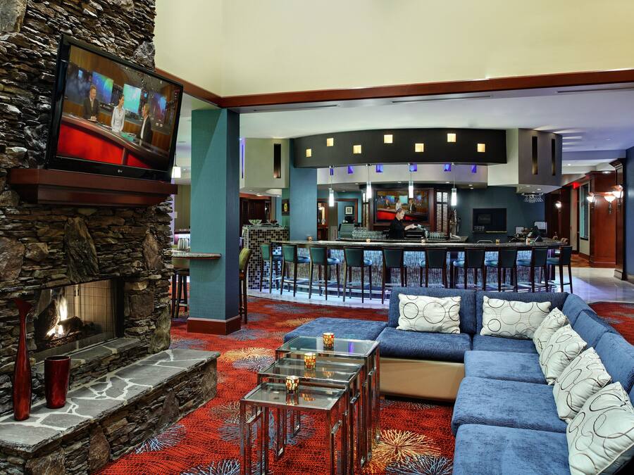 Un vestíbulo de hotel con chimenea de piedra, un sofá azul, una zona de bar y un espacio para comer.