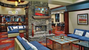 A lobby with a stone fireplace, sofas, a TV mounted on the wall, and a bar area in the background.