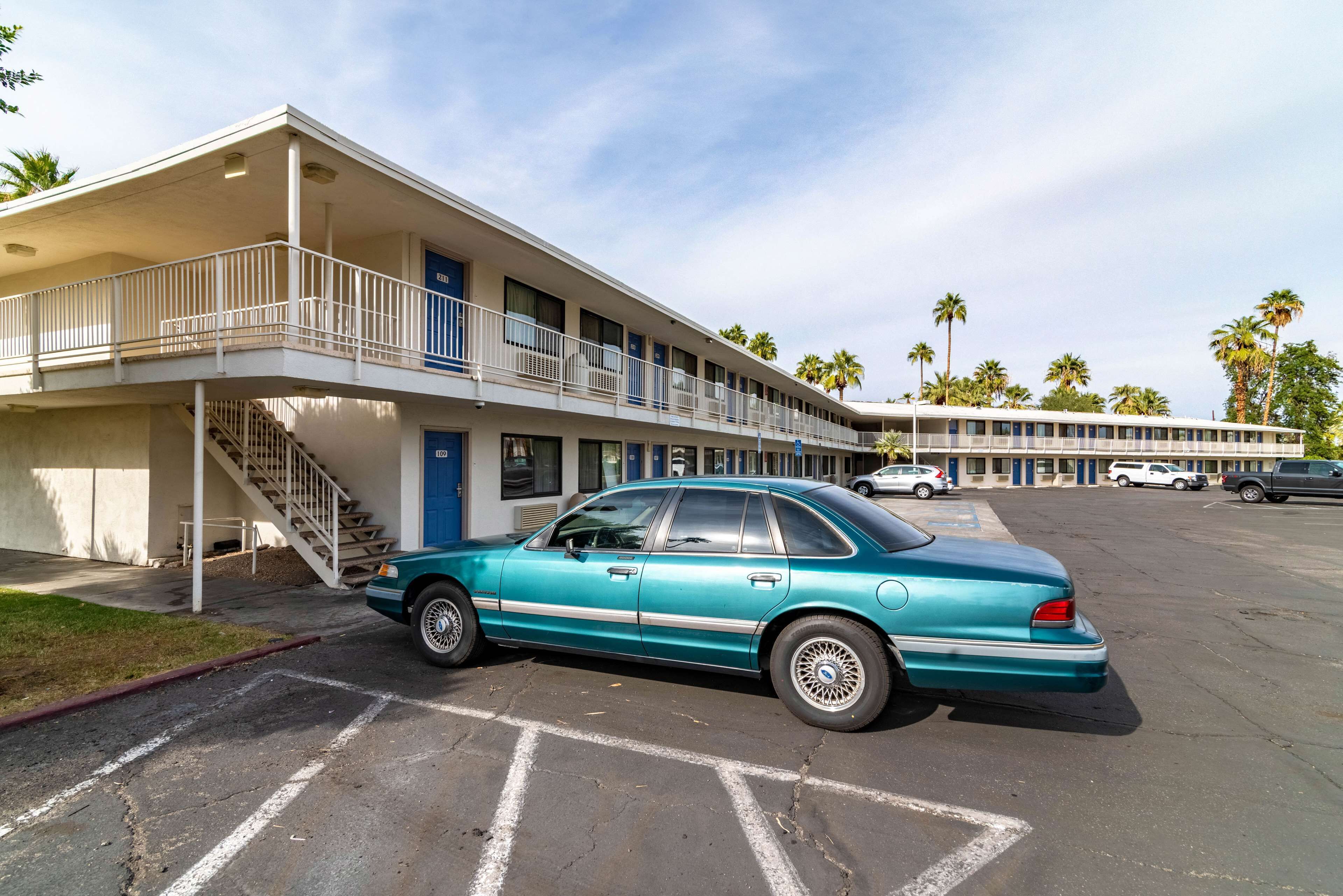 A motel with a two-story structure, a parking lot, and a turquoise car parked in front.