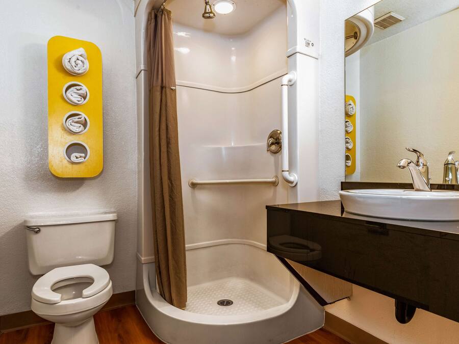 A bathroom with a white toilet, a shower with a beige curtain, a yellow wall-mounted soap dispenser, and a sink with a mirror above it.