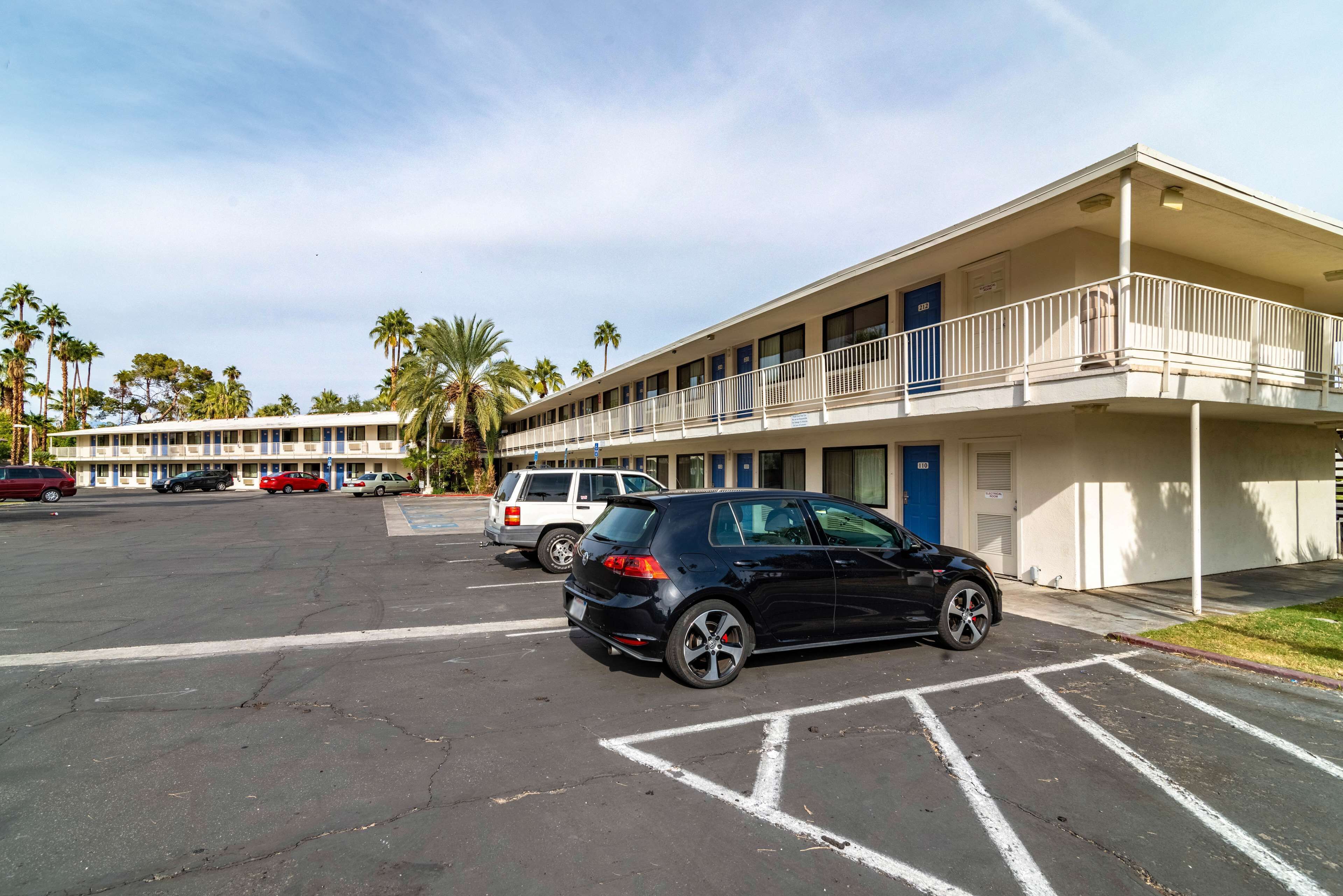 A motel with a parking lot, multiple cars, and palm trees in the background.