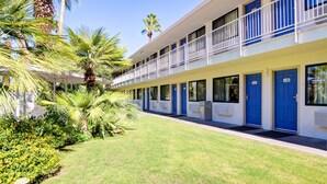 A motel with a covered outdoor area, multiple rooms with blue doors, and palm trees. - Motel 6 Palm Springs, CA - East - Palm Canyon (Palm Springs)