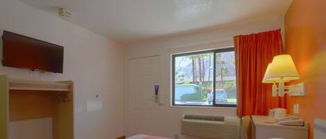 A hotel room with a bed, a TV, a window with curtains, a desk with a lamp, and a heater.