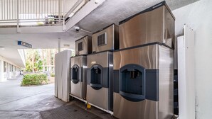 A row of stainless steel self-service beverage dispensers under a covered area with a sign indicating the office location. - Motel 6 Palm Springs, CA - East - Palm Canyon (Palm Springs)