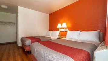 A hotel room with two beds, a nightstand with a lamp, and a heater.
