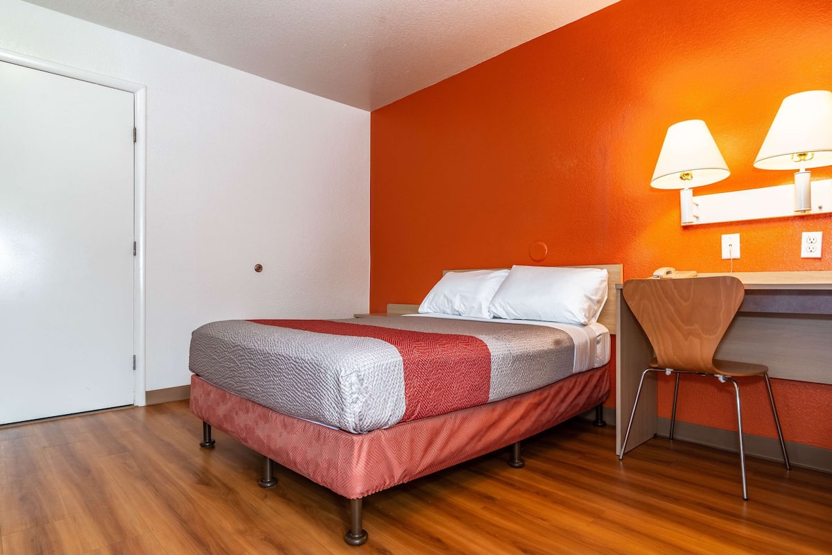 A bedroom with a bed, a chair, and a desk with lamps.