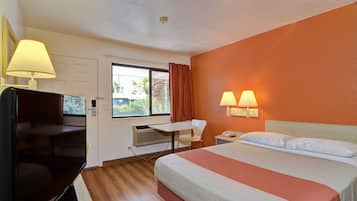 A hotel room with a bed, a desk, a chair, a TV, and two wall lamps.