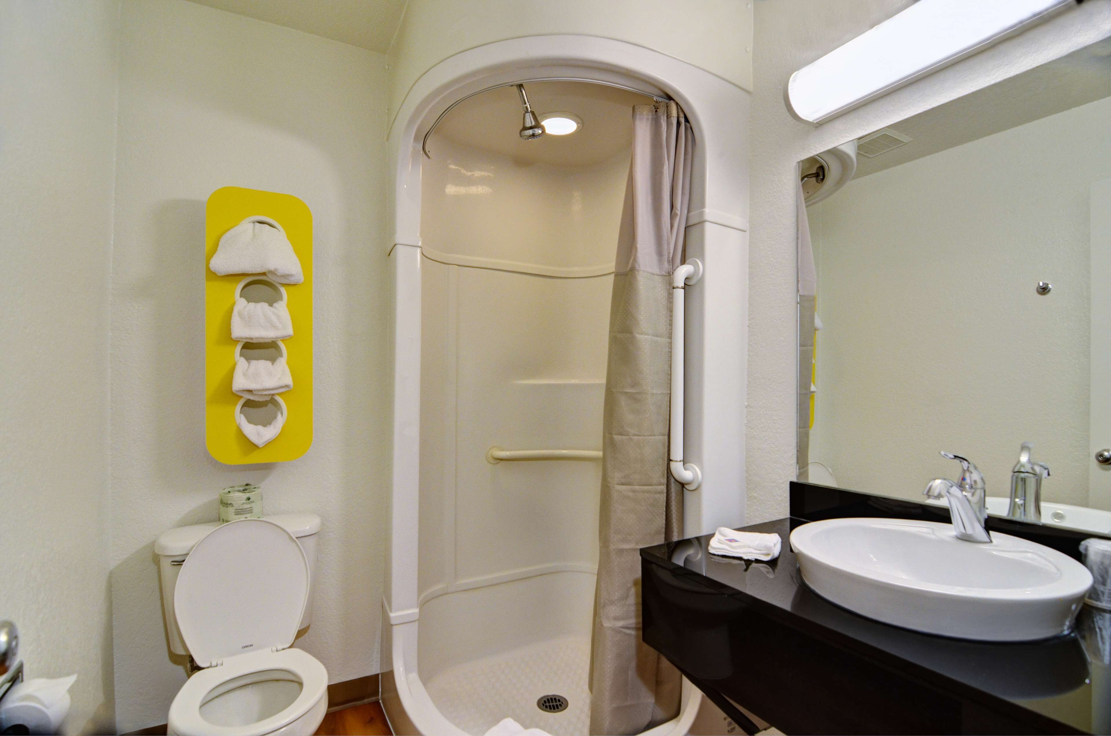 A bathroom with a white toilet, a shower with a beige curtain, a sink with a mirror, and a yellow towel rack.