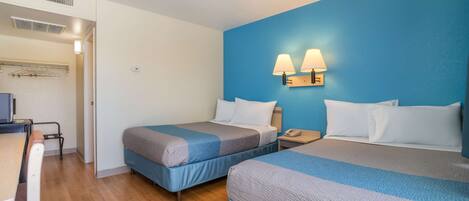A hotel room with two beds, a desk, and a chair.