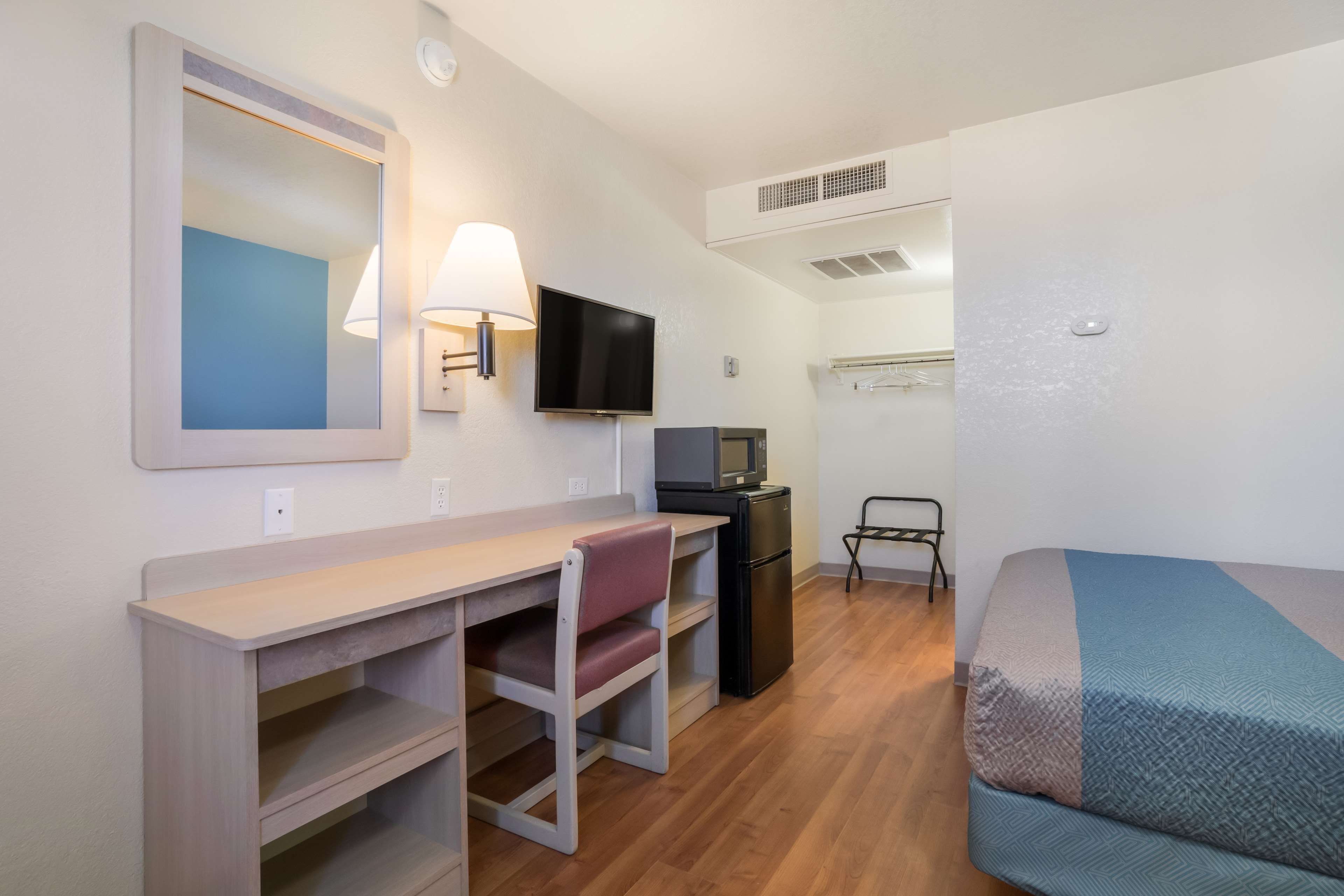 A compact hotel room with a bed, a desk with a chair, a television, and a small refrigerator.