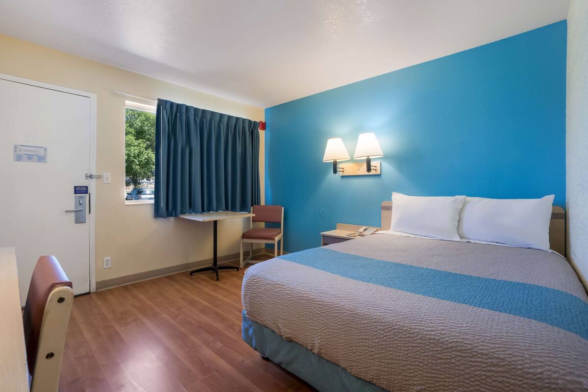 A hotel room with a bed, a desk, a chair, and a window with curtains.