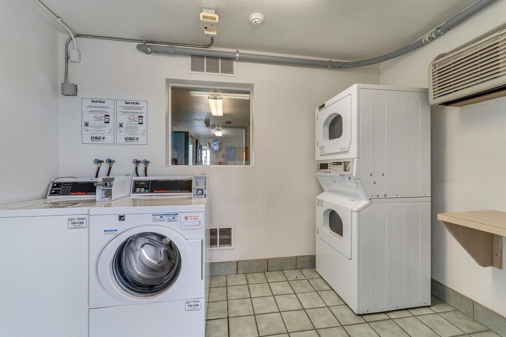 A laundry room with a front-loading washing machine, a stacked dryer, and a utility panel with service instructions.