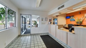 A reception area with a tiled floor, a reception desk, a computer, a clock, and a window with a view of the outside. - Motel 6 Grand Junction, CO (Grand Junction)