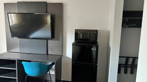 Cocina compacta con televisión de pantalla plana, microondas y pequeño comedor con una silla azul.