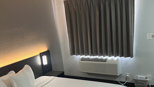 Habitación de hotel con una cama grande, una mesita de noche, aire acondicionado de pared y una ventana con cortinas.