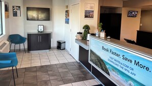 A reception area with a desk, chairs, a TV, and a poster advertising a booking service. - Motel 6 Lakeland, FL (Lakeland)