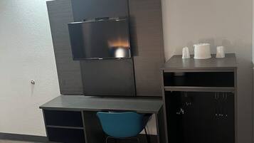 Una habitación moderna con un escritorio, una silla azul, un televisor montado en la pared y un mueble bajo con tazas.
