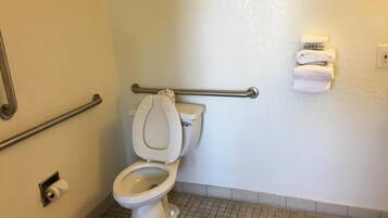 Un baño estándar con inodoro, barras de apoyo, toallero y porta papel higiénico.