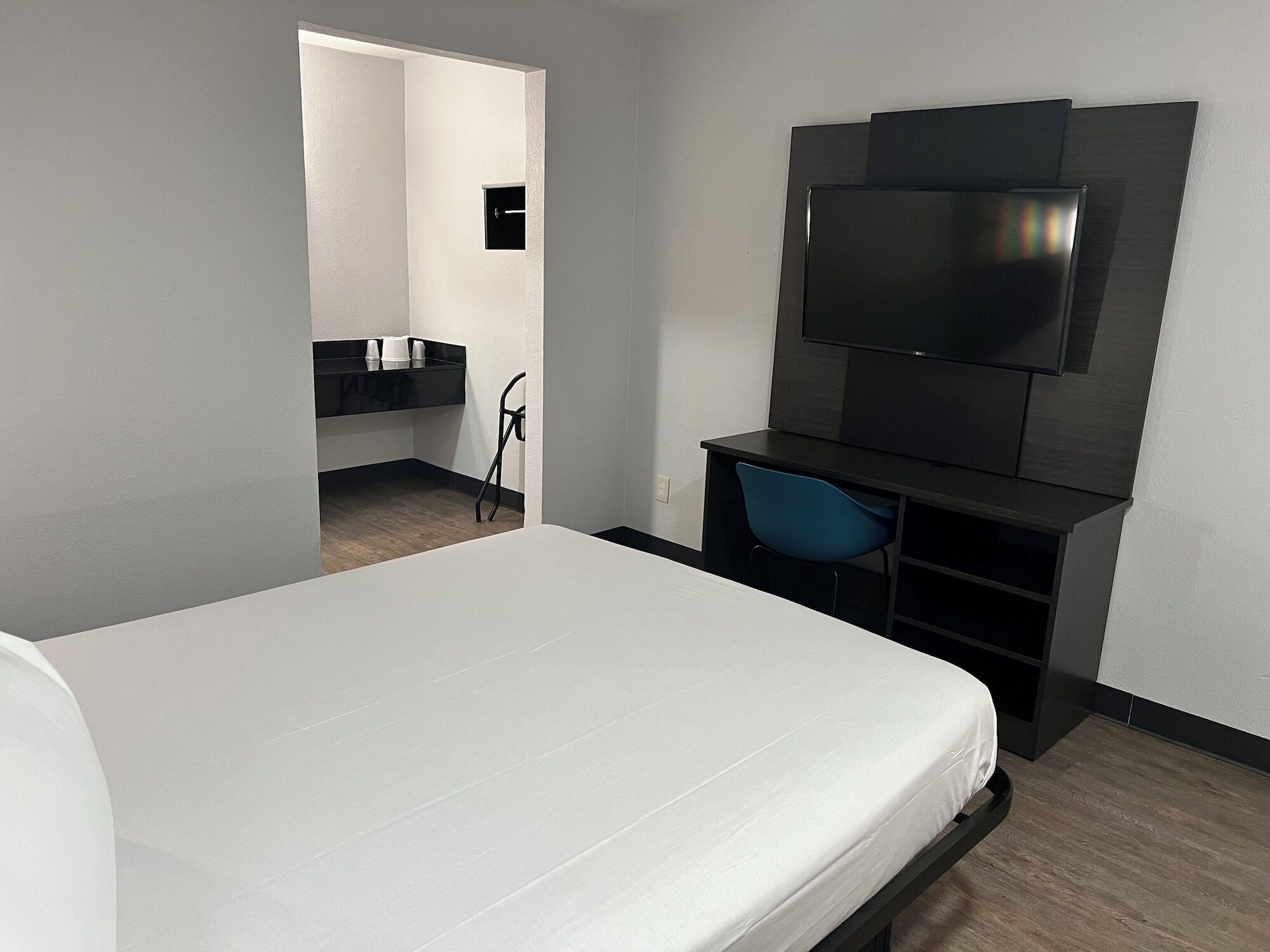 A modern hotel room with a large bed, a TV mounted on the wall, a desk with a chair, and a small bathroom area.