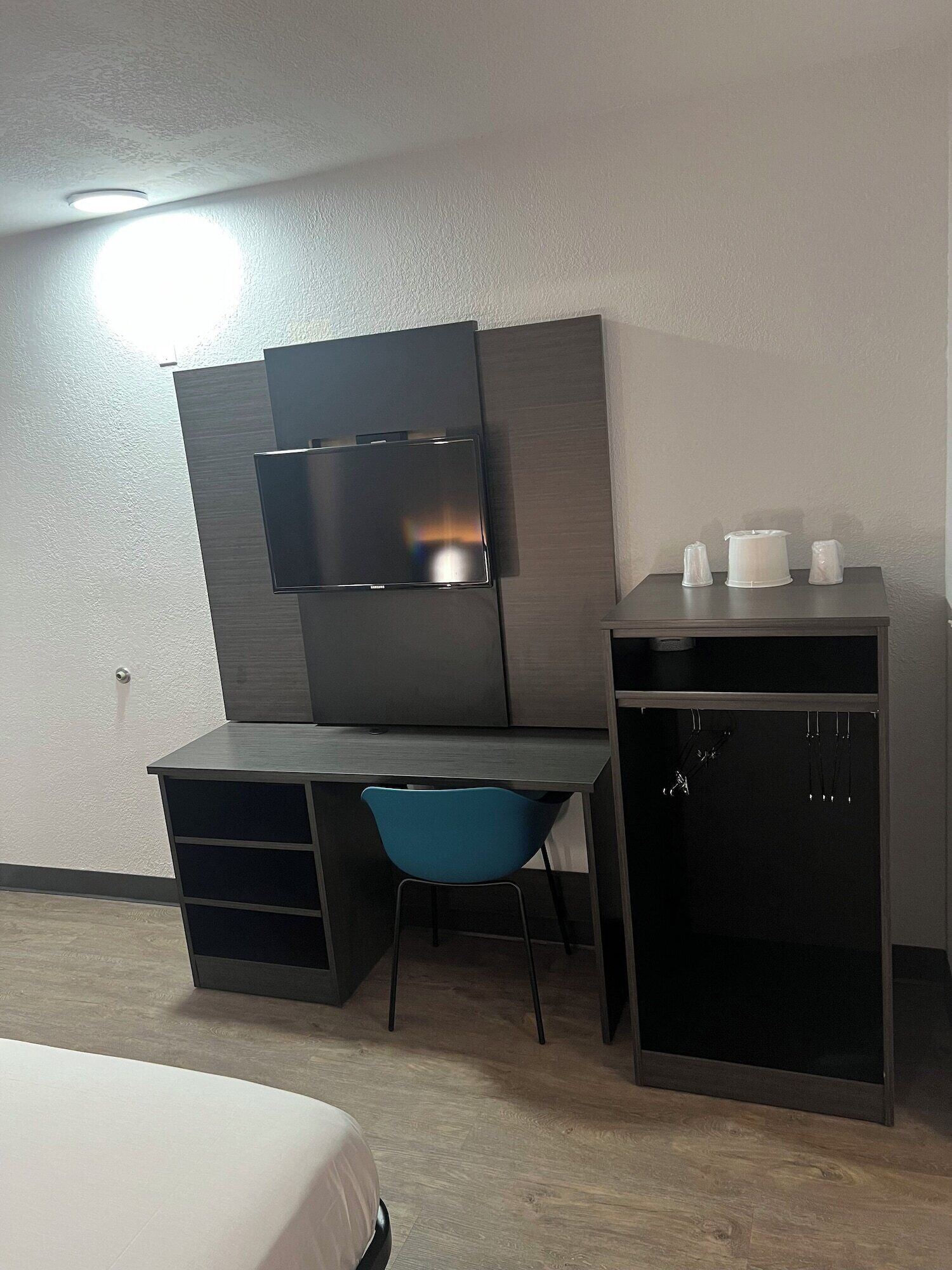 A modern room with a desk, a blue chair, a TV mounted on the wall, and a small cabinet.
