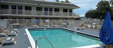 A pool area with lounge chairs and a building with multiple balconies.