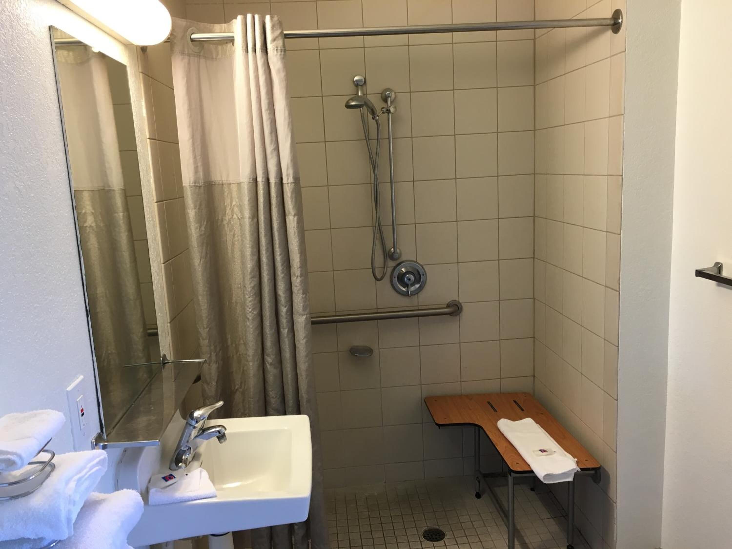 Une petite salle de bain compacte, équipée d’une douche, d’un lavabo et d’un banc en bois.