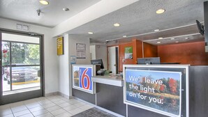 Zona de recepción de un hotel con un mostrador, un ventanal amplio y un cartel que indica que es un Motel 6.