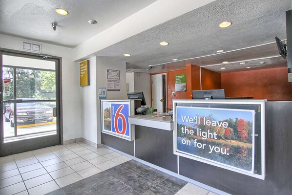 Zona de recepción de un hotel con un mostrador, un ventanal amplio y un cartel que indica que es un Motel 6.