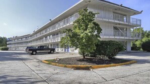 Un hotel de varios pisos con un patio central, un estacionamiento y un vehículo estacionado al frente.