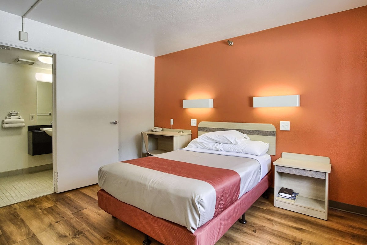 Ein Hotelzimmer mit Bett, Nachttischen, einem Spiegel und einem durchgegangene Tür sichtbaren Badezimmer.