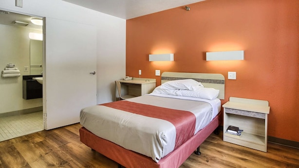 Habitación de hotel con cama, mesitas de noche, espejo y baño visible a través de una puerta abierta.