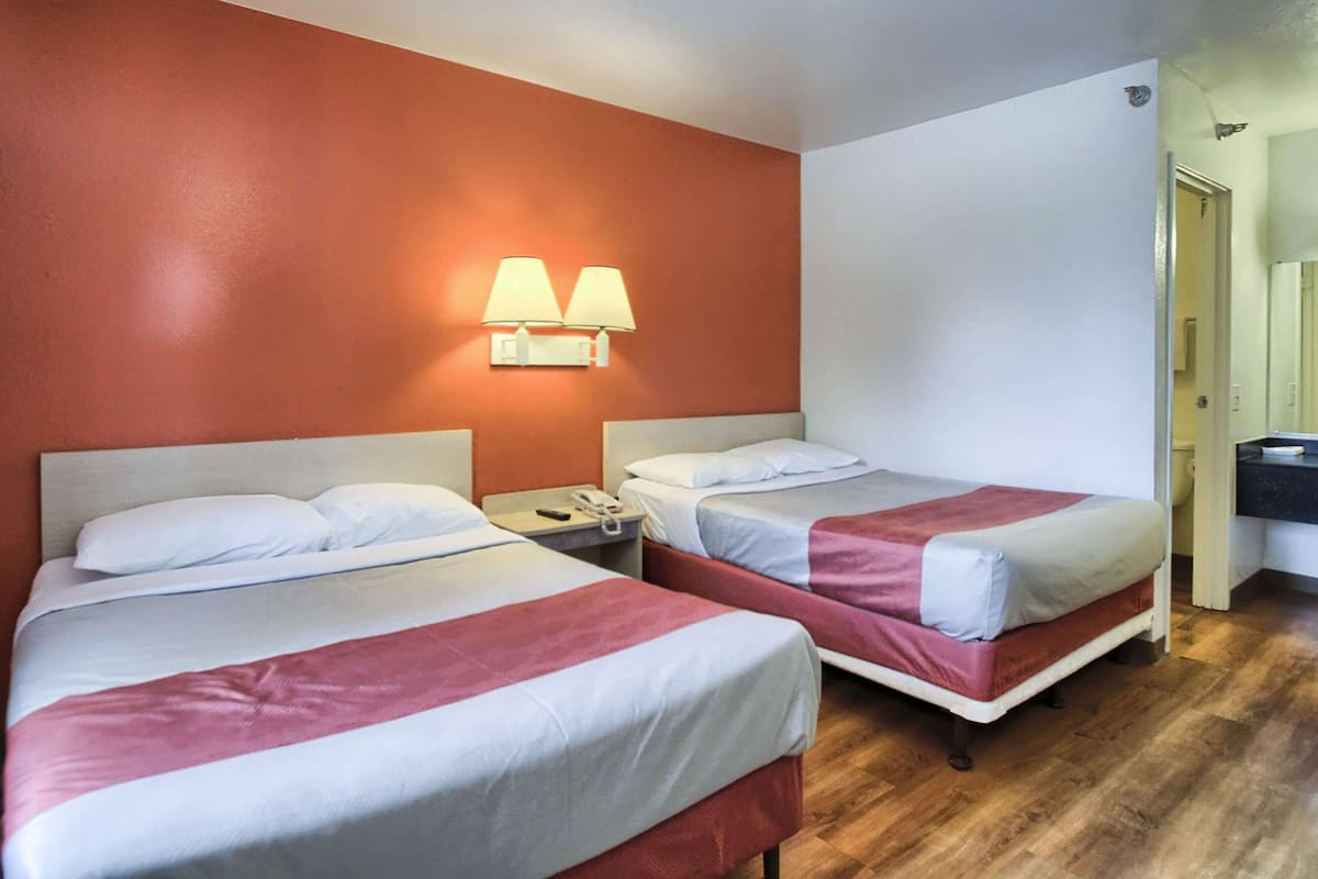 Ein Hotelzimmer mit zwei Betten, einem Nachttisch und einem durchgegangenen Tür sichtbar liegenden Badezimmer.