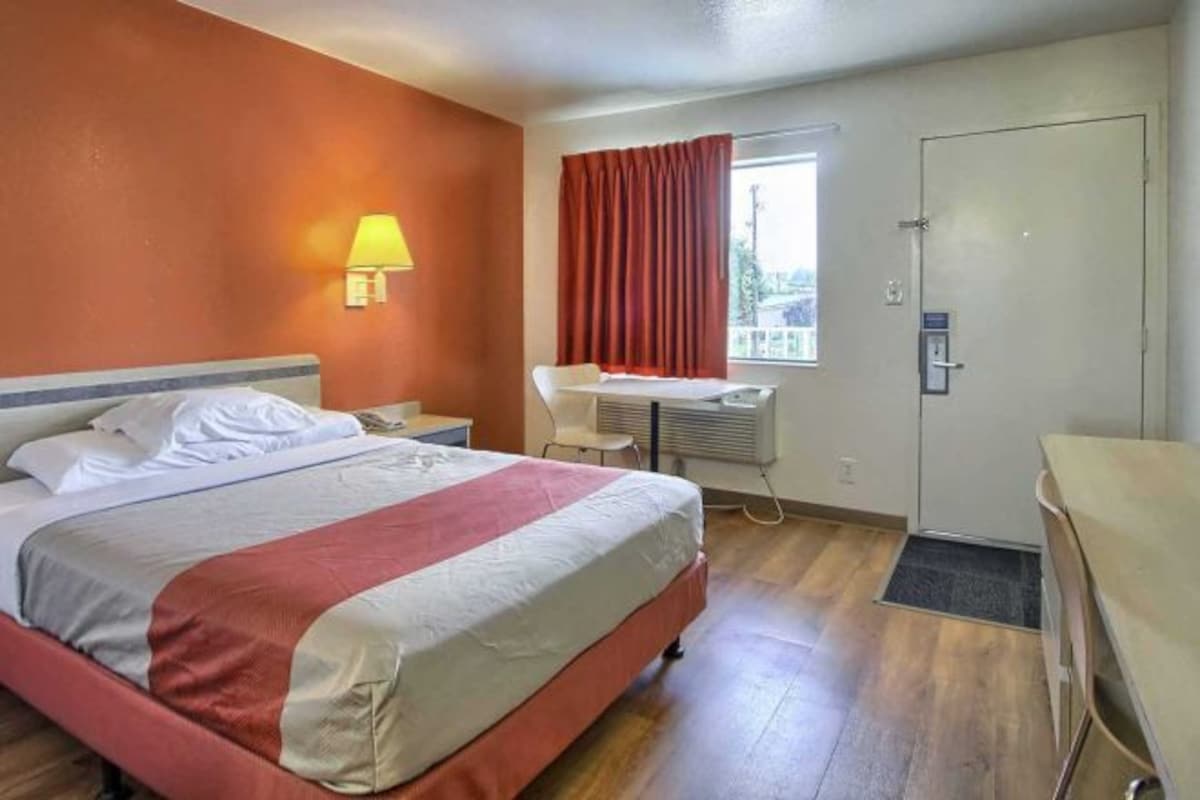 Une chambre d’hôtel avec un lit, un bureau, une chaise, une fenêtre avec des rideaux et une porte.