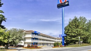 Un motel con un letrero que dice '6', indicando que pertenece a la cadena 6. Tiene un letrero de 'Bienvenido' sobre la entrada y un letrero que dice 'Wi-Fi disponible'.