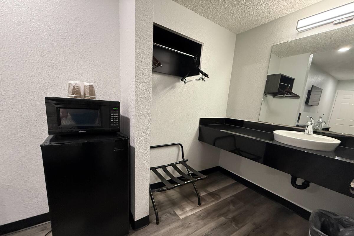 A compact bathroom with a black refrigerator, a microwave, a sink, and a mirror.