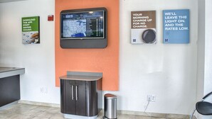 A reception area with a digital weather display, a trash bin, and informational posters on the wall. - Motel 6 Seattle, WA - South (SeaTac)