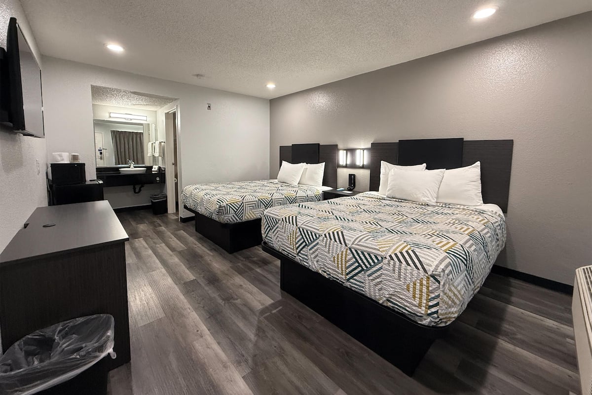 A hotel room with two beds, a desk, a mirror, and a bathroom visible through an open door.