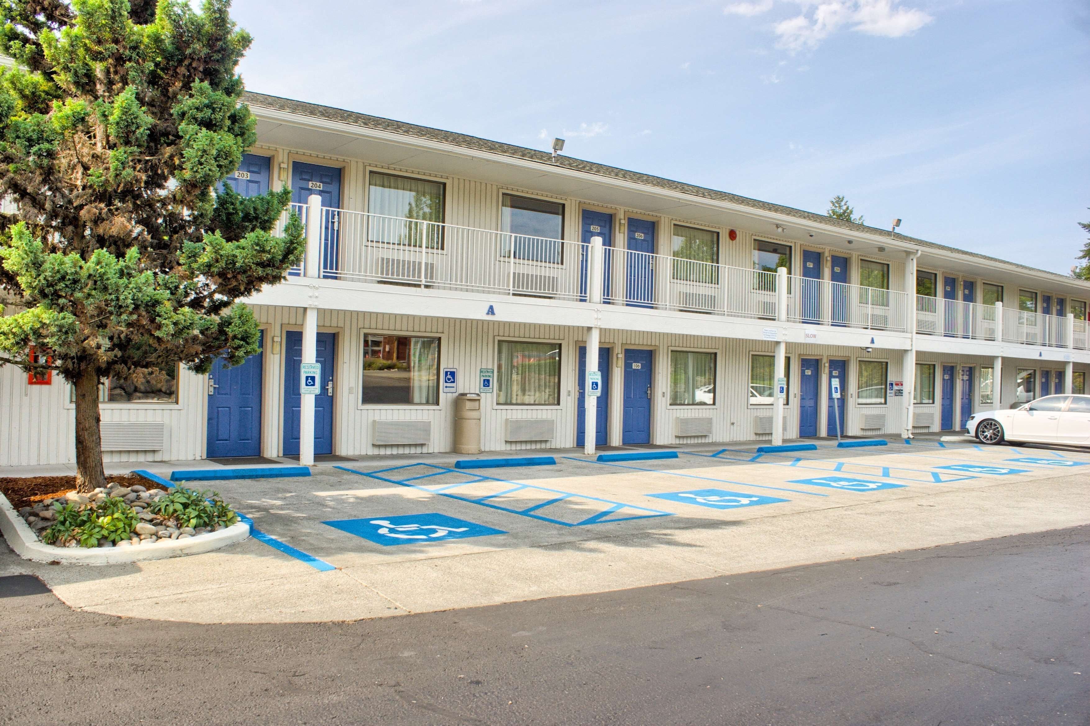 Un motel doté de plusieurs chambres, d’un parking et d’un arbre.