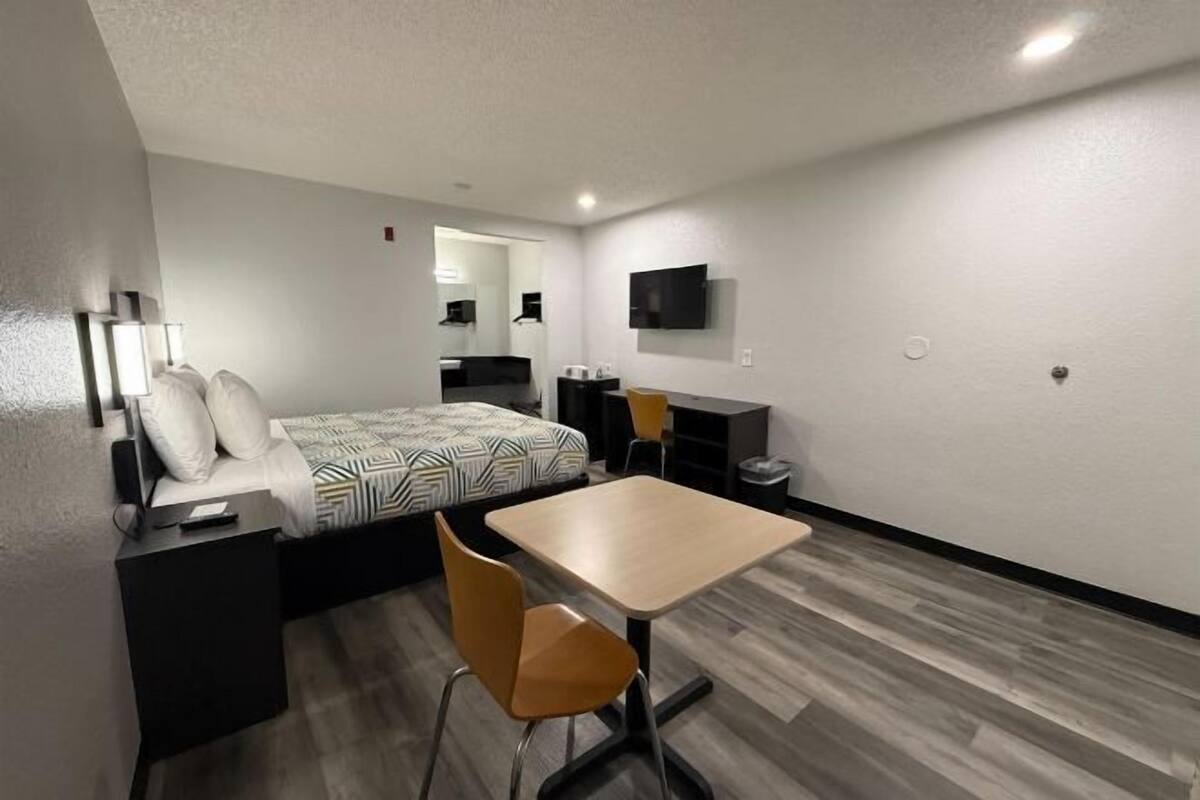 A modern hotel room with a bed, a desk, a chair, a TV, and a mirror.