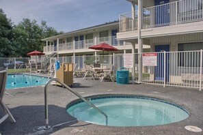 A pool area with lounge chairs and umbrellas, a fenced pool, and a building with multiple balconies.