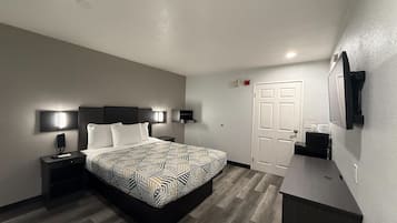 A modern hotel room with a large bed, bedside tables, a desk, a mirror, and a door.