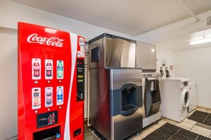 A room with a red Coca-Cola vending machine, a stainless steel refrigerator, and a washing machine.