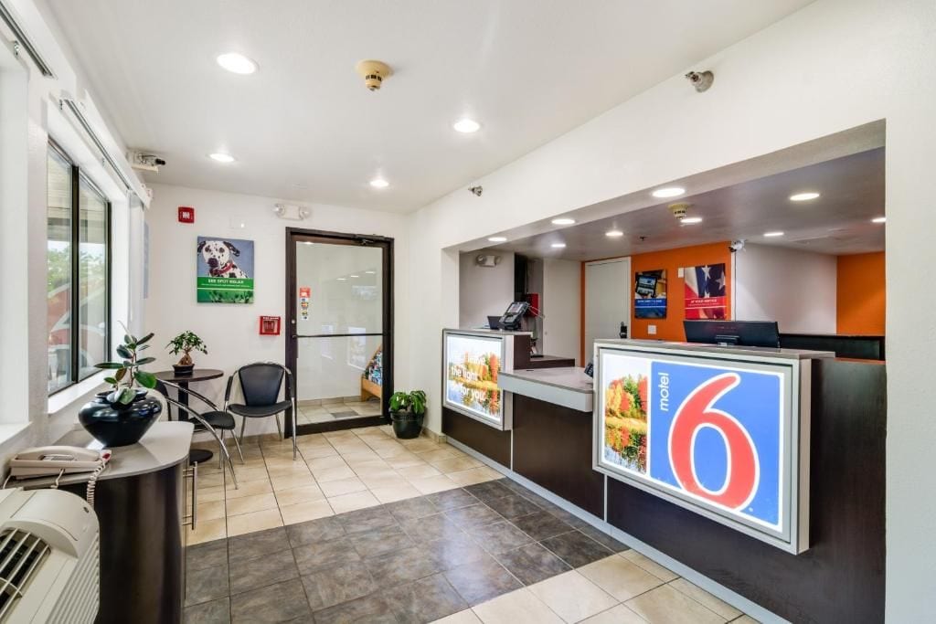 A hotel reception area with a reception desk, a phone, a plant, a chair, and a poster advertising a motel.