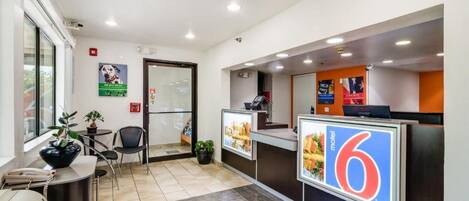 A hotel reception area with a reception desk, a phone, a plant, a chair, and a poster advertising a motel.