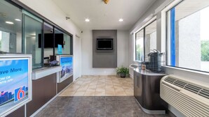 A reception area with a flat-screen TV, a digital sign, a potted plant, and a built-in air conditioning unit. - Motel 6 Rolling Meadows, IL - Chicago Northwest (Rolling Meadows)