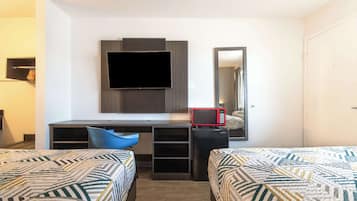 A hotel room with two beds, a desk with a flat-screen TV, a microwave, and a mirror.